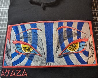 May include: Black hooded sweatshirt with an embroidered design of stylized eyes. The eyes have blue and white striped backgrounds, red outlines, and yellow and orange details. Japanese text is below the eyes.