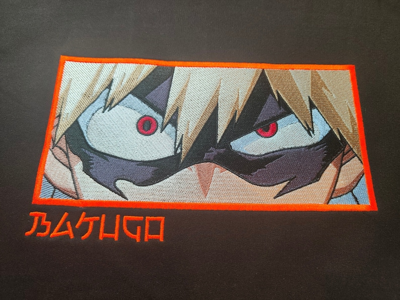 May include: A close-up of an embroidered image of a character with spiky blonde hair and red eyes. The character is wearing a black mask and has a serious expression. The image is surrounded by an orange border and the text "BAKUGO" is below the image.