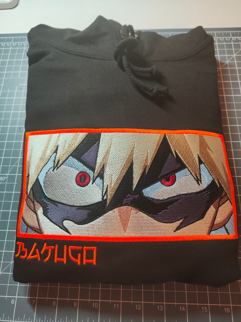 May include: Black hoodie with an orange embroidered image of an anime character with red eyes and the text "乃ムケムGロ" in orange.