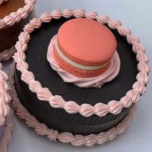 Peut inclure: Un gâteau noir avec du glaçage rose et un macaron rose sur le dessus.