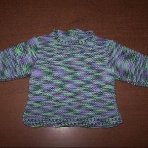 Peut inclure: Pull en tricot fait à la main dans les tons de vert, violet et bleu. Le pull a des manches longues et un col et un ourlet côtelés. Le fil a un motif de couleurs variées, créant un aspect texturé. Le pull est probablement pour un bébé ou un tout-petit.