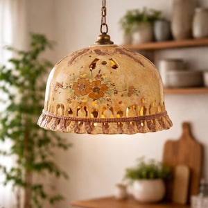 May include: A dome-shaped ceramic pendant light fixture featuring a cream-colored glaze with hand-painted orange floral motifs. The shade includes intricate cut-out patterns along the lower edge and is suspended by a metallic chain.