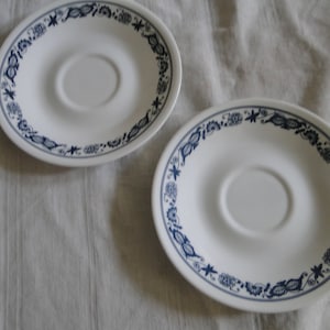 Puede incluir: Dos platillos de cerámica blanca con un patrón floral azul alrededor del borde.