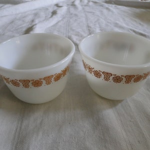 May include: Two white ceramic mugs with brown floral designs around the rim.