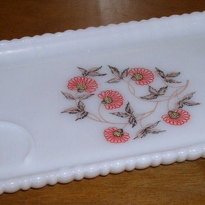 May include: White milk glass serving tray with a beaded edge and a floral design in shades of pink and brown. The tray has a small, round indentation in the center.
