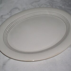 May include: White oval serving platter with a silver rim and three concentric silver lines.