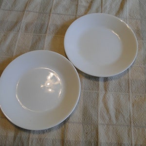 May include: Two white ceramic plates, one slightly larger than the other, are placed on a beige checkered tablecloth.