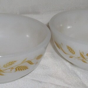May include: Two white ceramic bowls with a gold wheat design. The bowls are empty and have a smooth, glossy finish.