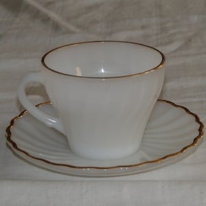 Puede incluir: Una taza de té y un platillo blancos con un borde dorado. La taza y el platillo están hechos de un material liso y opaco.