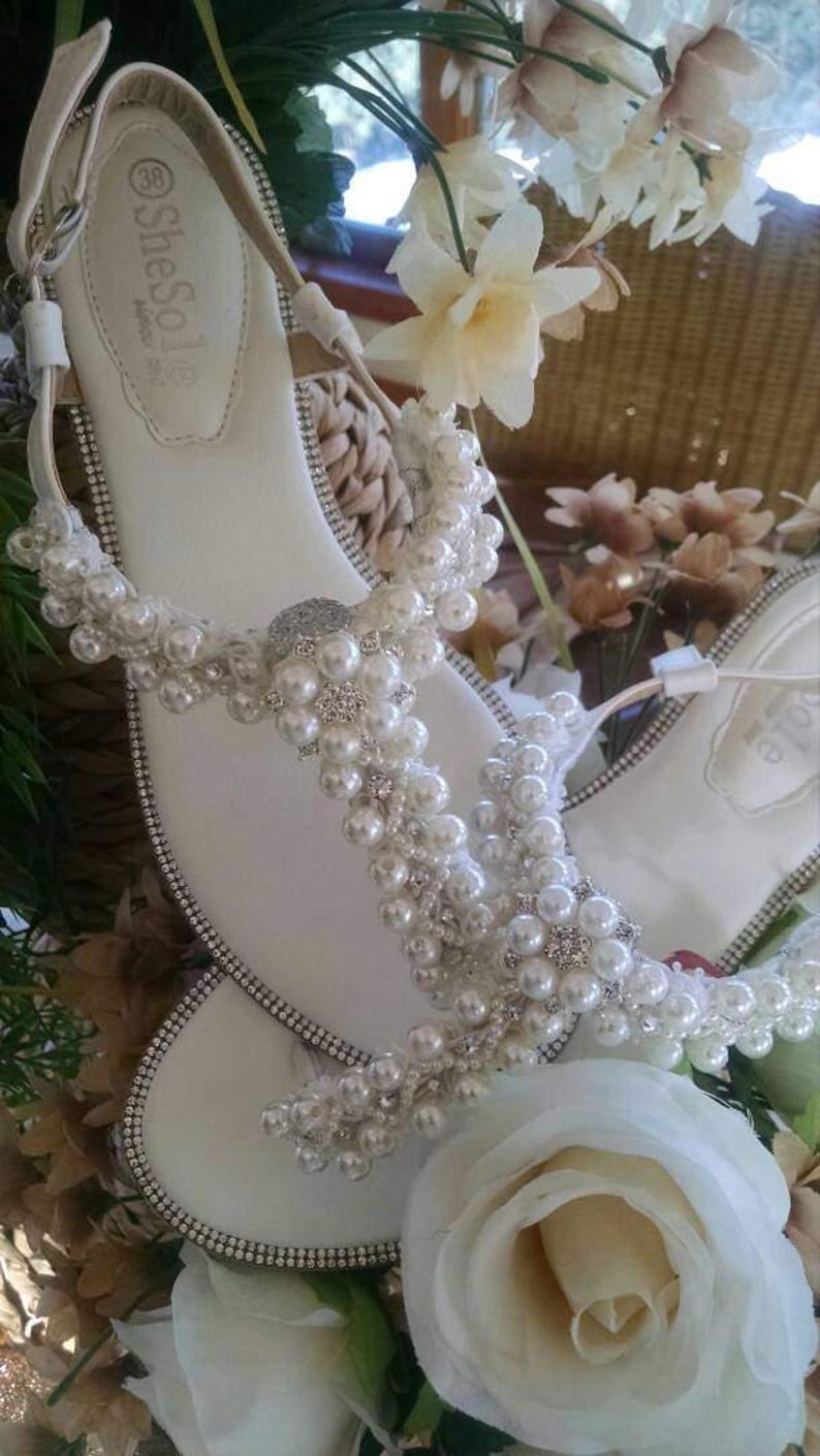 K&ouml;nnte beinhalten: Wei&szlig;e Sandalen mit Perlen- und Strassbesatz. Die Sandalen haben ein schlichtes Design und sind perfekt f&uuml;r eine Sommerhochzeit oder einen anderen besonderen Anlass.