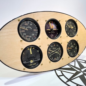May include: A wooden oval-shaped wall clock with a black trim and five round analog gauges. The gauges have black faces with white numbers and markings. The gauges are labeled "Air Speed", "Direction", "Climb", and "2 Min Turn".