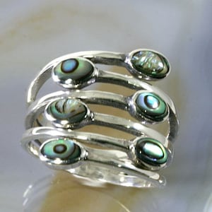 Könnte beinhalten: Ein silberner Ring mit fünf ovalen Einlagen aus Abalone-Muschel. Der Ring besteht aus mehreren Bändern, die sich um den Finger wickeln.