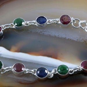 Könnte beinhalten: Ein silbernes Armband mit einem Kettenglieddesign und runden Edelsteinen in Blautönen, Grün- und Rottönen.