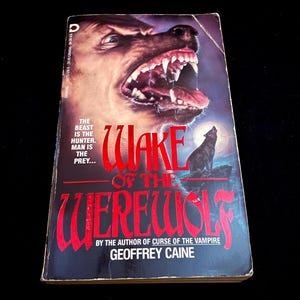 May include: A paperback book titled "Wake of the Werewolf" by Geoffrey Caine. The cover features a snarling werewolf head with bared teeth and a howling wolf silhouette under a full moon. The text "The beast is the hunter. Man is the prey..." is also visible.