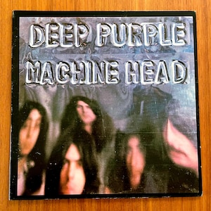 May include: Album cover for Deep Purple's "Machine Head." The album art features the band's name and album title in a raised, metallic font. The background shows a blurred image of the band members. The cover is framed in black.