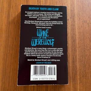 May include: The back cover of a paperback book titled "Wake of the Werewolf" by Abraham Stroud. The cover is black with white and blue text, including the title and a synopsis of the story. The ISBN and barcode are visible.