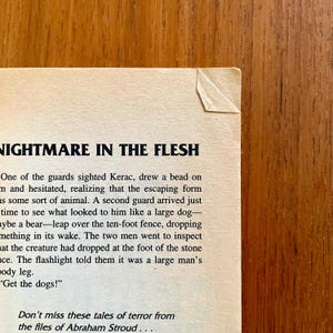May include: A close-up of a book page with the title "NIGHTMARE IN THE FLESH" in bold black letters. The text describes a suspenseful scene with guards and a mysterious creature. The page has a torn corner.