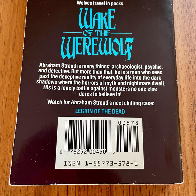 May include: The back cover of a book titled "Wake of the Werewolf" with a dark background and teal text. The text includes a synopsis of the book's plot and the ISBN. The book is about a man who battles monsters.