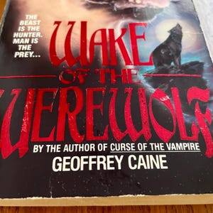 May include: A book cover for "Wake of the Werewolf" by Geoffrey Caine. The title is in large, red, stylized letters. A black wolf howls at the moon. The cover has the text "The beast is the hunter. Man is the prey..."