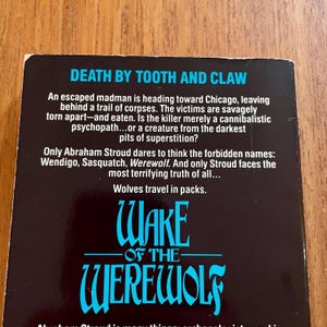 May include: A book cover with the title "Death by Tooth and Claw" in white text on a black background. Below, the title "Wake of the Werewolf" is in blue, stylized lettering. The cover text describes a story involving a madman, corpses, and werewolves.