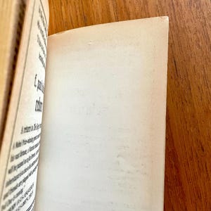 May include: Open book with aged, off-white pages. The left page has printed text in black ink. The right page is blank. The book is open on a wooden surface.