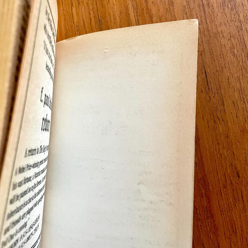 May include: Open book with aged, off-white pages. The left page has printed text in black ink. The right page is blank. The book is open on a wooden surface.
