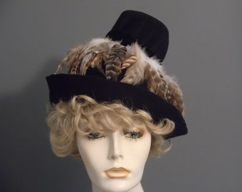 May include: A black felt hat with a tall crown and a wide brim. The hat is decorated with a cluster of brown and white feathers.