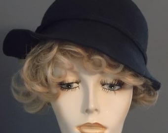 Puede incluir: Un sombrero cloche de fieltro negro con un ala ancha y un diseño sencillo. El sombrero lo lleva un maniquí con el pelo rubio y rizado.