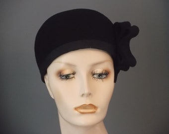 May include: A black felt cloche hat with a large black felt bow on the side.