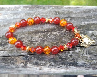 May include: A red and orange beaded bracelet with a gold fox charm. The bracelet is made with carnelian and amber beads.