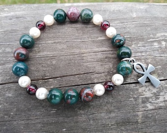 May include: A green, red, and white beaded bracelet with a silver Ankh charm. The bracelet is made with natural stones and pearls.