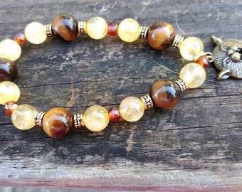 May include: A brown and gold beaded bracelet with a tiger's eye and citrine stone design. The bracelet has a metal charm in the shape of a wolf's head.