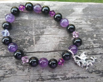 May include: A black and purple beaded bracelet with a silver dragon charm. The bracelet is made with round black and purple beads, and small clear crystal beads.