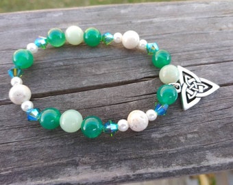 May include: A green and white beaded bracelet with a silver Celtic knot charm. The bracelet is made with jade, white beads, and crystal beads.