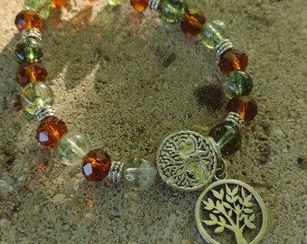 May include: A green and amber beaded bracelet with two silver tree of life charms. The bracelet is on a gray textured surface.