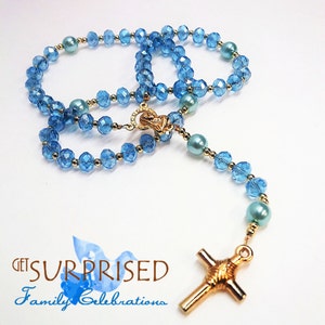 May include: A blue crystal rosary with gold accents and a gold cross. The rosary has light blue and white beads.