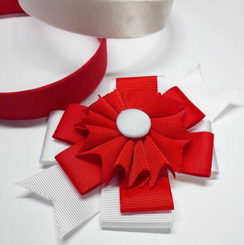 May include: A red and white bow with a white button in the center. The bow is made of ribbon and is perfect for adding a touch of elegance to any occasion.