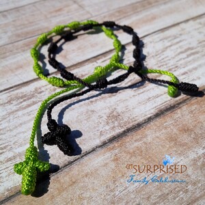 May include: Black and green knotted rope necklace with two cross pendants. The cross pendants are made of the same knotted rope.