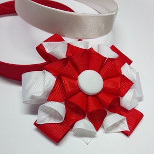 May include: A red and white fabric flower with a white center, attached to a red headband and a white headband.