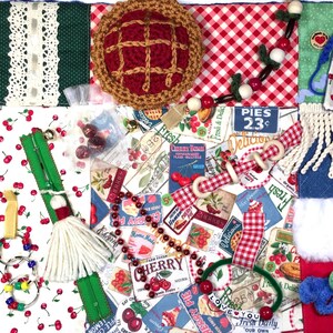 May include: A sensory activity quilt featuring a cherry-patterned fabric, a crocheted pie, wooden beads, a green zipper with a white tassel, a white fringe, a faux fur patch, and a pocket with a tag reading: BELONGS TO: Insert your loved one's name in pocket.