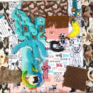 May include: A sensory activity mat featuring a dog-themed fabric border with various attached tactile elements including a turquoise crochet chain, a yellow silicone fidget toy, wooden beads, a brown faux fur square, and a pocket with the text BELONGS TO: Insert your loved one's name in pocket.