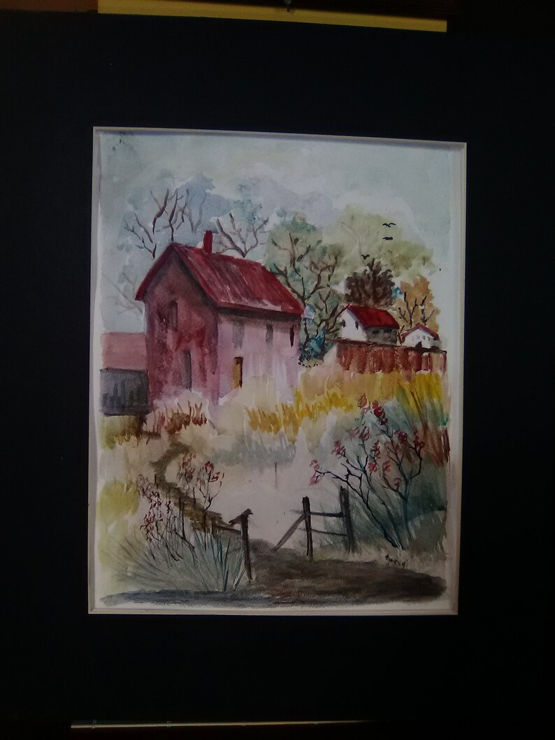 May include: Watercolor painting of a red-roofed house with a fence in front of it. The house is surrounded by trees and bushes. The painting is framed in black.