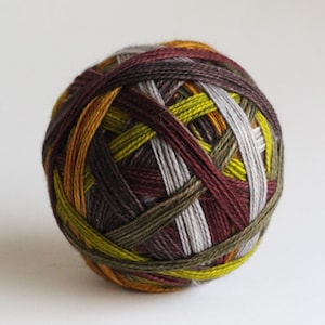 May include: A spherical ball of yarn featuring a variegated color palette of deep burgundy, olive green, mustard yellow, and light grey. The strands are tightly wound in a crisscross pattern, creating a textured surface with distinct color transitions.