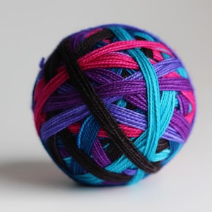 May include: A ball of colorful yarn in shades of black, pink, purple, and blue. The yarn is tightly wound, creating a textured sphere. Ideal for knitting, crocheting, or other fiber crafts.