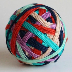 May include: A colourful ball of yarn, featuring a woven pattern. The yarn incorporates shades of red, teal, purple, navy, and beige. The yarn is tightly wound, forming a spherical shape. Ideal for knitting and crochet projects, this yarn is a crafter's delight.