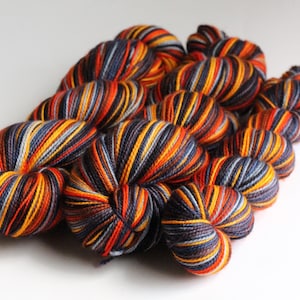 May include: A collection of colorful yarn skeins. The yarn features a striped pattern with shades of orange, yellow, navy blue, and gray. The skeins are arranged in a cluster, showcasing the texture and color variations of the yarn. Ideal for knitting and crochet projects.