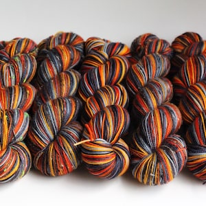 May include: Close-up of several skeins of yarn in a variety of colors. The yarn is a mix of orange, yellow, black, and gray. The yarn is tightly wound and ready for use in knitting or crochet projects.
