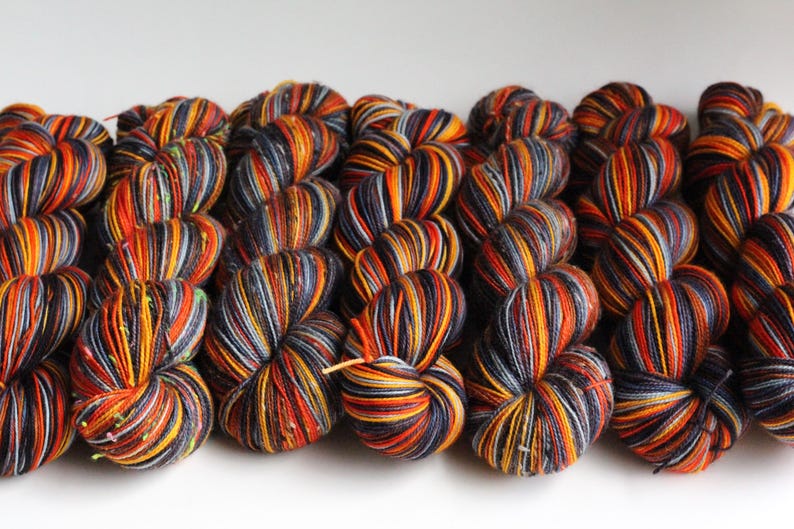 May include: Close-up of several skeins of yarn in a variety of colors. The yarn is a mix of orange, yellow, black, and gray. The yarn is tightly wound and ready for use in knitting or crochet projects.