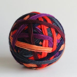Puede incluir: Una madeja de hilo colorido con hebras entrelazadas. El hilo presenta una mezcla de colores, incluyendo naranja, rojo, morado y azul oscuro. Esta madeja de hilo es adecuada para proyectos de tejido y ganchillo.