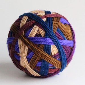 May include: A ball of yarn with a woven pattern of various colors, including purple, blue, brown, and beige. The yarn is tightly wound, creating a spherical shape. This yarn is suitable for knitting and crocheting projects.
